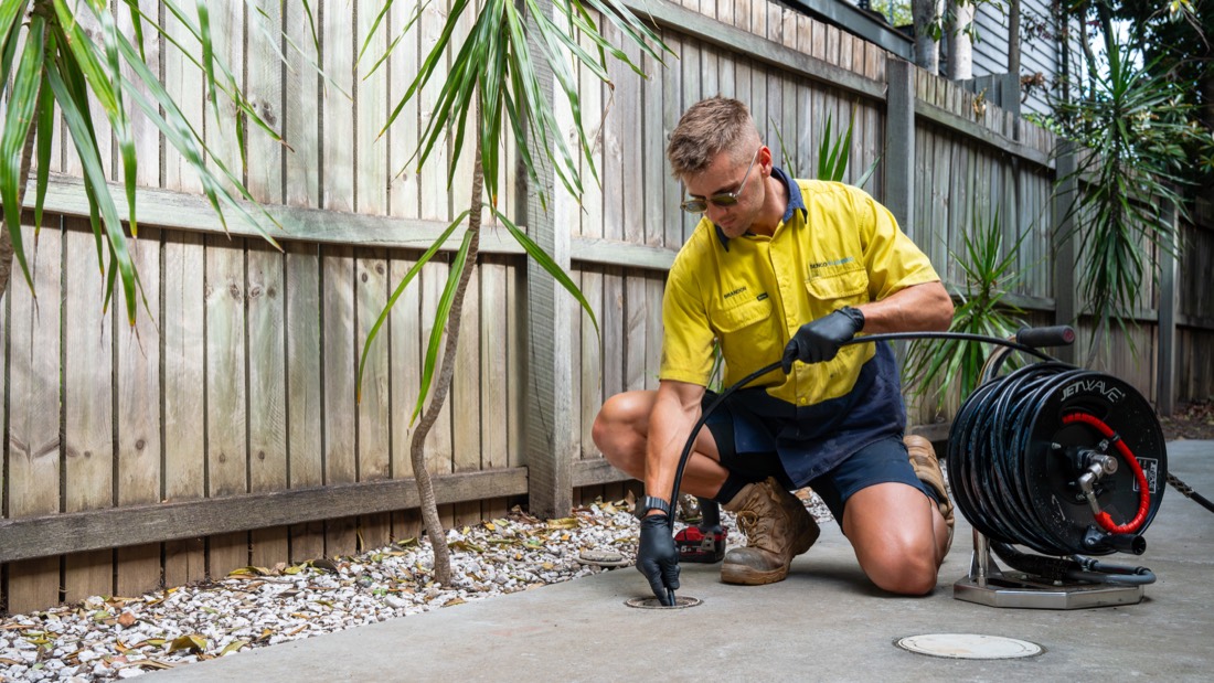 Senco Plumbing technician feeding a high-pressure drain line into a ground drain to clear a blockage in Northgate, Brisbane